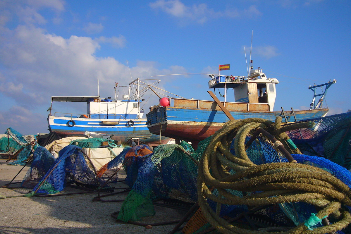 El descanso de los barcos
Andaluc&iacute;a se ha significado hist&oacute;ricamente por la importancia de sus &nbsp;astilleros y carpinter&iacute;as de ribera para la fabricaci&oacute;n de barcos. De esa industria apenas quedan algunos testigos aislados, pero los barcos siguen necesitando sus per&iacute;odos de descanso, para lo cual en cada puerto pesquero existen instalaciones donde varar las embarcaciones: al menos una vez al a&ntilde;o, el pescador ha de faenar en seco. Esto significa limpiar el caso de &ldquo;escaramujo&rdquo;, pasar la patente, pintar, arreglar desperfectos, revisar la mec&aacute;nica y equipos hidr&aacute;ulicos&hellip;., en definitiva, disimular el paso del tiempo y del esfuerzo sobre las herramientas de trabajo. La mayor parte de estas tareas son realizadas por los mismos tripulantes de las embarcaciones. Algunos varaderos, como el de Atunara (La L&iacute;nea de la Concepci&oacute;n), nos permiten disfrutar de la plasticidad que resulta del varamiento de los buques custodiados por los artes de rastro para la pesca del corruco, la principal pesquer&iacute;a en esta localidad.